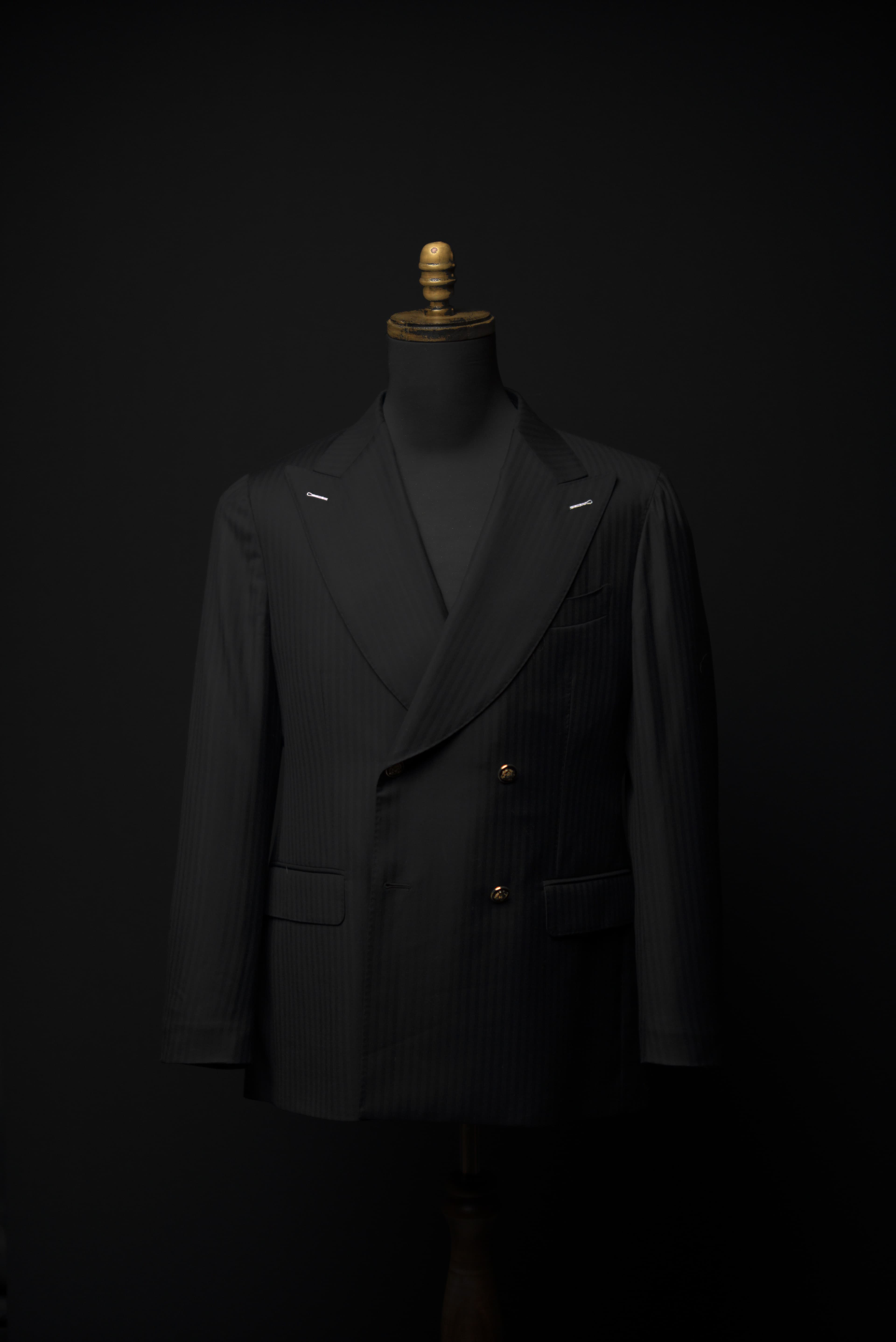 Black herringbone · double-breasted · six-button bronze metal · peak lapel · homepage hero anchor